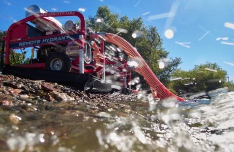 Red industrial vehicle with hose taking water from lake