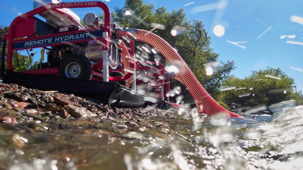 Red industrial vehicle with hose taking water from lake