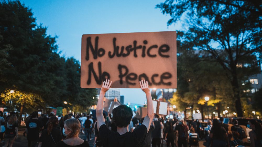 a photo of a protest with one person holding up a cardboard sign that reads No Justice No Peace