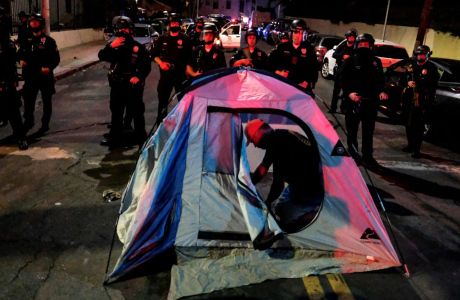 Man setting up tent in street in front of police officers