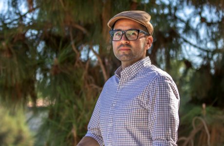 Man in cap and glasses outdoors in front of trees