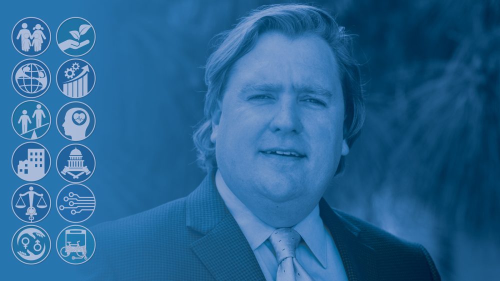 Headshot of a man wearing a suit with a blue overlay.