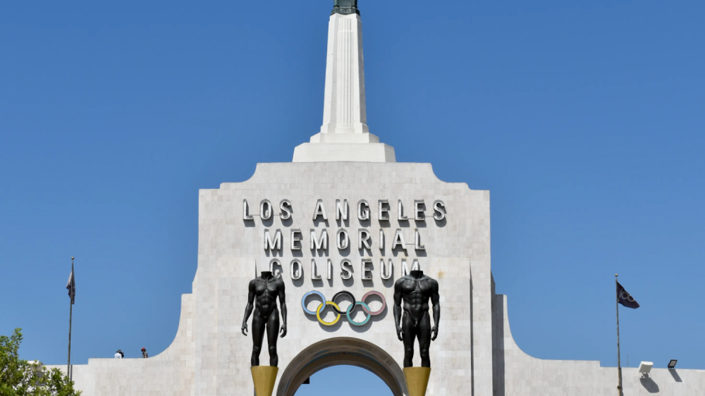 top of white building with spire and Olympic Games logo