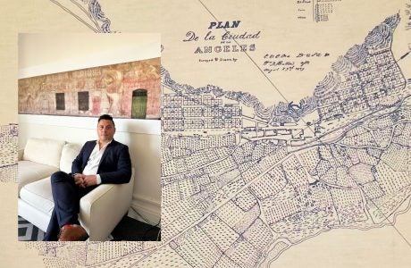 Photo of Edgar Garcia sitting on a couch over a large map of Los Angeles.|||||Edgar Garcia sits behind a desk holding up a piece of paper with a black and white photo and words that say "A Mexican Street of Yesterday in a City of Today"||Edgar Garcia, Urban Planning alum, sits at a desk in his office holding up a photo map of El Pueblo de Los Angeles.