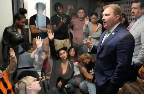 Man in suit speaks to room filled with young people