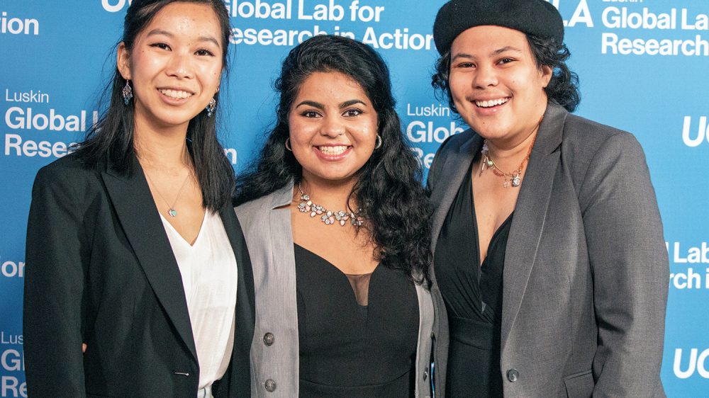 three young people smile in front of UCLA backdrop