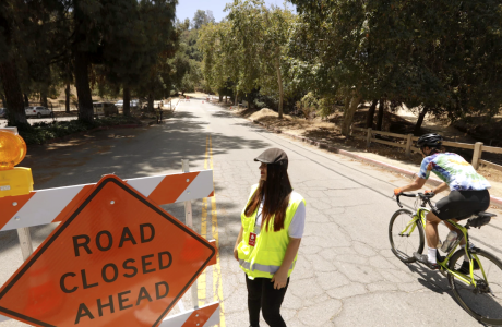 bicyclist on wooded road next to road closure sign and woman in yellow safety vest