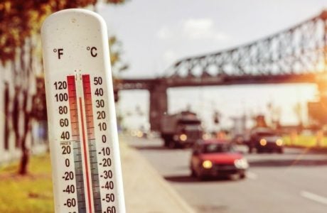 Thermometer reads 100 degrees Fahrenheit with cars driving on a street in the background
