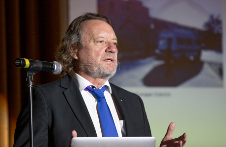 man with beard speaks at podium|image shows flags from various nations|illustration of a triangle illustrates the three key measurement areas of the report