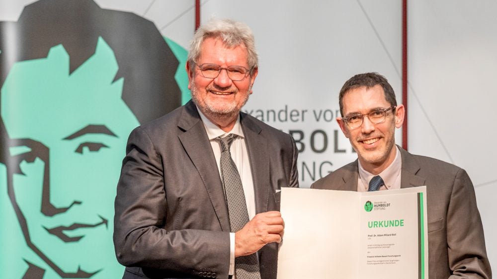 Two men holding paper folder holding award statement