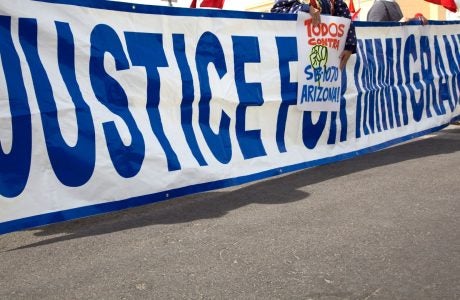 A group holds up a long sign that says Justice for Immigrants at a rally on the street.