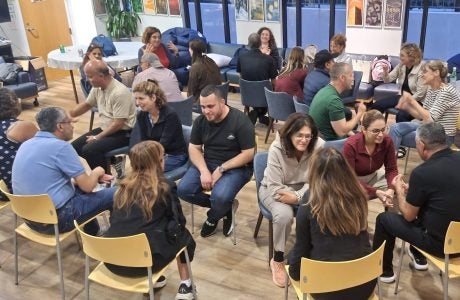 Visiting educators sit in concentric circles for one-on-one conversations|Woman holds small art collage with lyric "there is a crack in everything, that's how the light gets in."|Large group of people pose outdoors|Group works on art project on outdoor patio|Man in glasses delivers lecture