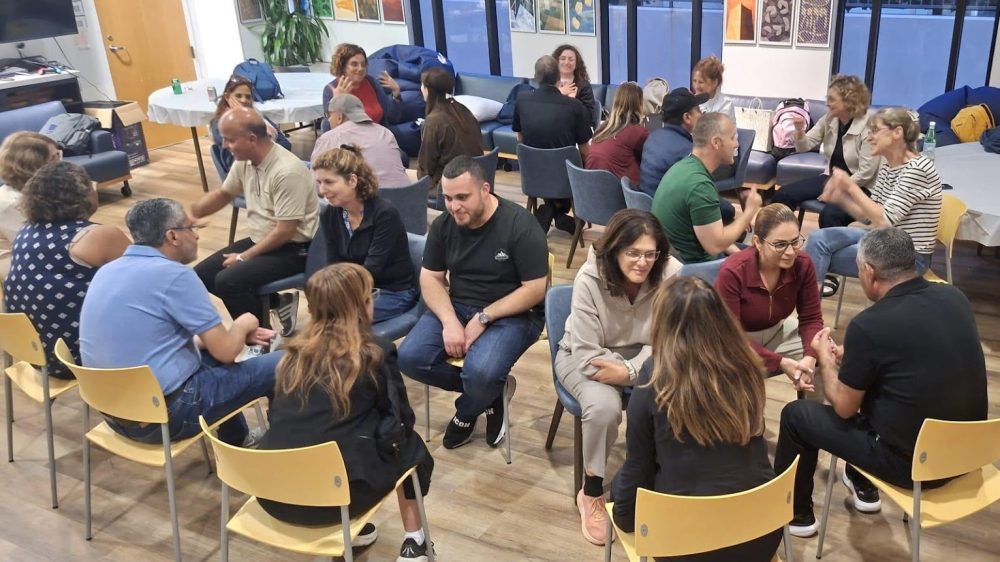 Visiting educators sit in concentric circles for one-on-one conversations|Woman holds small art collage with lyric "there is a crack in everything, that's how the light gets in."|Large group of people pose outdoors|Group works on art project on outdoor patio|Man in glasses delivers lecture