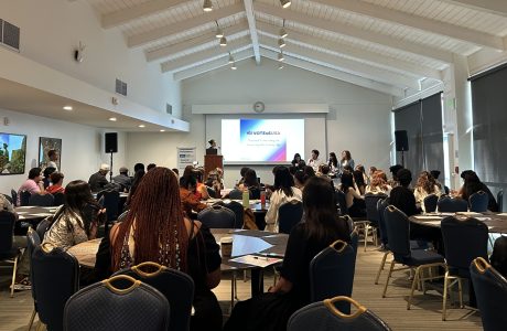 Large conference area with circle tables, dozens of youth seated while someone on stage does a presentation.