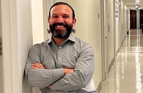 man smiles as he stands beneath sign that designates office location for research hub