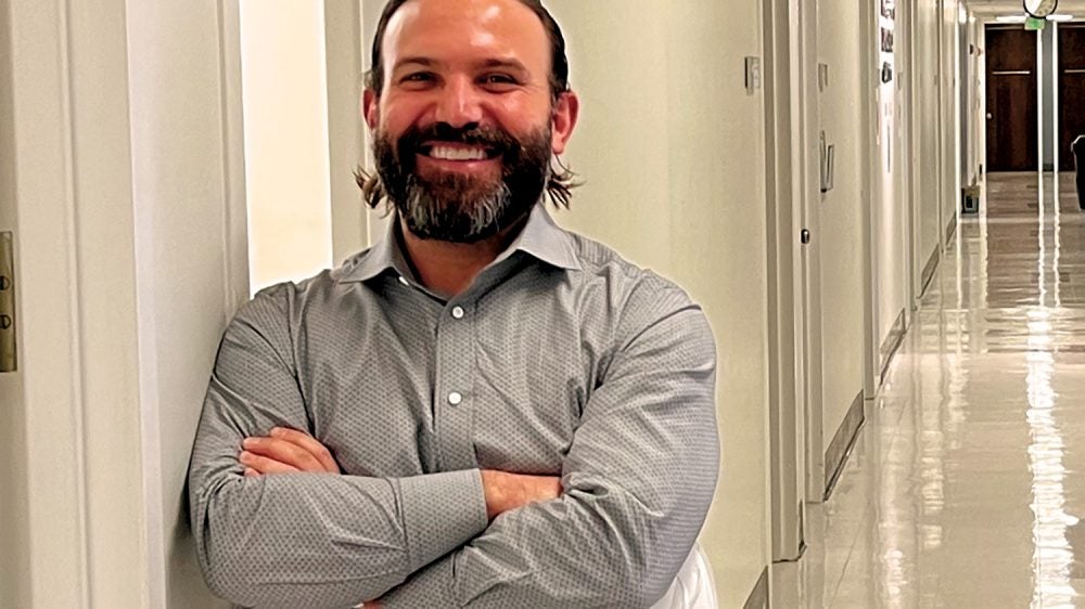 man smiles as he stands beneath sign that designates office location for research hub