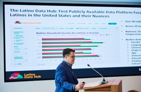 man in blue suit talks at podium with a chart on screen behind him