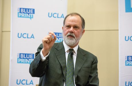 main in suit and tie gestures in front of backdrop showing UCLA and Blueprint logos|