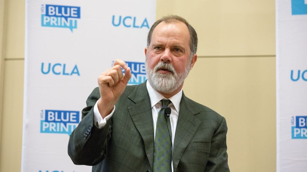 main in suit and tie gestures in front of backdrop showing UCLA and Blueprint logos|