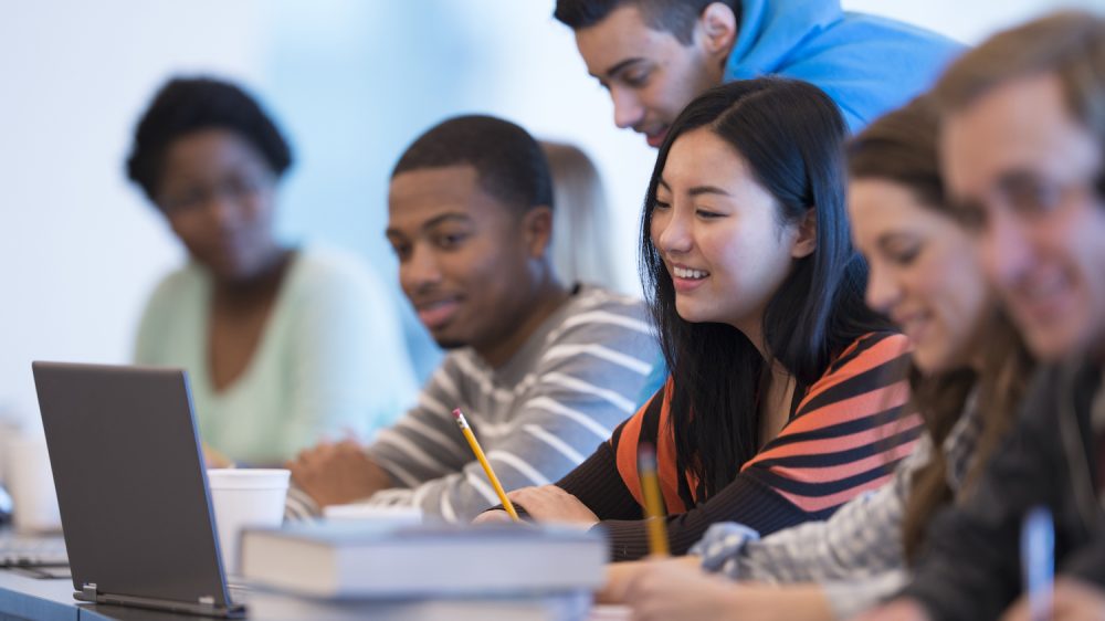 Young people at a desk with books and laptop