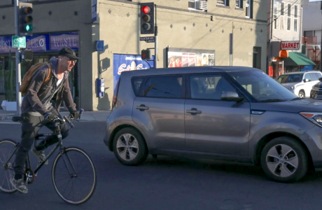 man on bicycle next to car on city street
