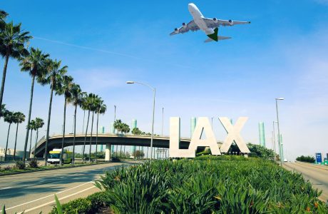 Photo of LAX sign with an airplane flying overhead at the los angeles airport.