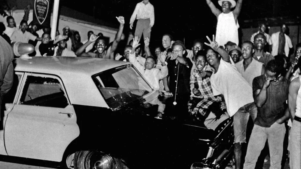 In this Aug. 12, 1965 file photo, demonstrators push against a police car after rioting erupted in the Watts district of Los Angeles. It began with a routine traffic stop 50 years ago this month, blossomed into a protest with the help of a rumor and escalated into the deadliest and most destructive riot Los Angeles had seen. The Watts riot broke out Aug. 11, 1965 and raged for most of a week. When the smoke cleared, 34 people were dead, more than a 1,000 were injured and some 600 buildings were damaged.
