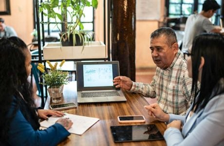 Three people at table in coffee shop with laptop open