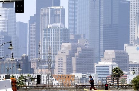 Photo of a man jogginb across the street with the background of Los Angeles cityscape in the scorching heat