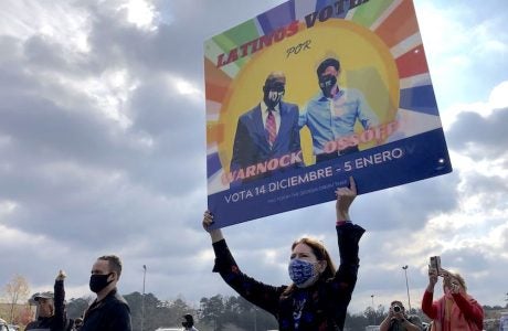 woman in mask holding multicolored sign to get out the vote