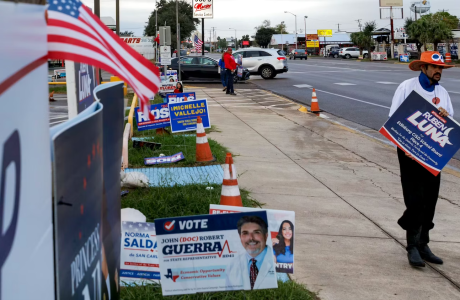 Man in orange hat on street with many campaign signs