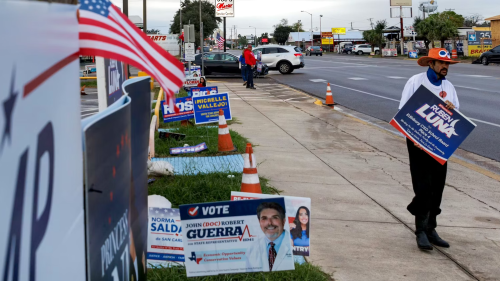 Man in orange hat on street with many campaign signs