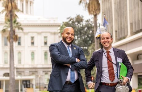 two men in suits pose with state Capitol building behind them