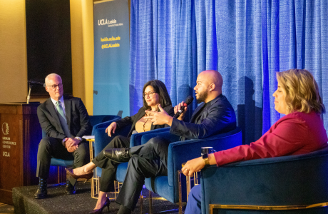 four people in business attire site on a stage and chat with a blue background behind them|||||