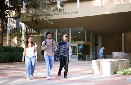 Photo of three students walking in front of the UCLA Luskin School of Public Affairs building.