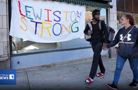 two people holding hands in front of "Lewiston Strong" banner|