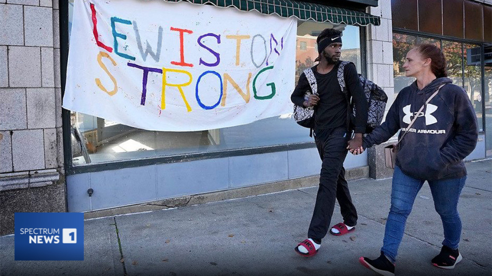 two people holding hands in front of "Lewiston Strong" banner|