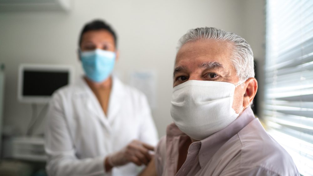 Portrait of nurse applying vaccine on patient's arm using face mask