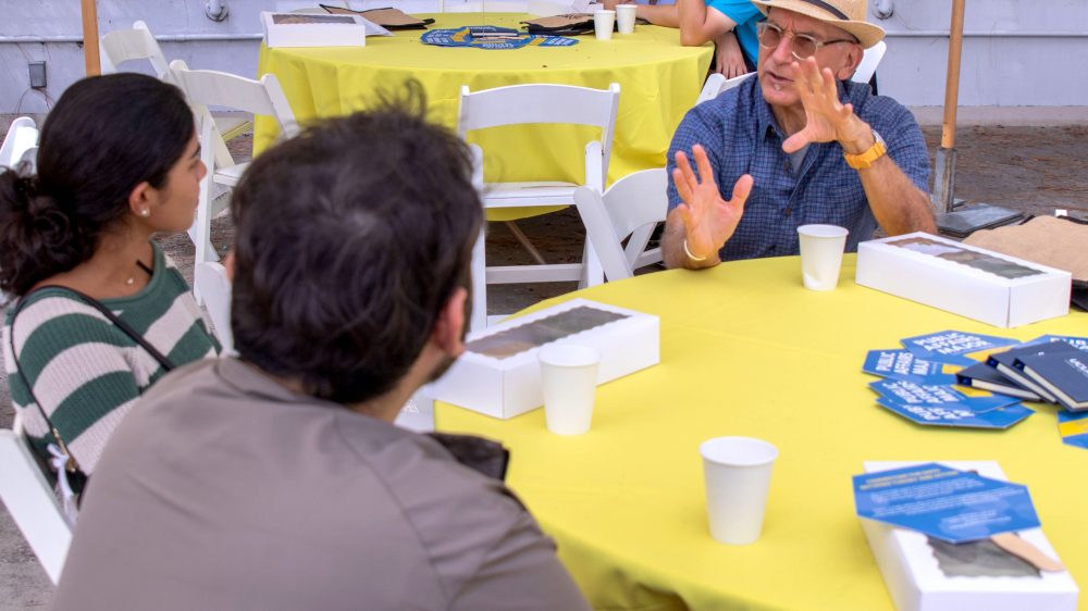 Man in glass and hand sits at table with two students|Man in white shirt and dark jacket standing at festive table