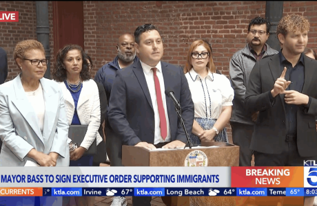 Mayor Karen Bass stands next to Edgar Garcia, MURP '06 who is at the pulpit introducing the mayor as she signs a new executive directive to protect immigrant communities amid ICE raids happening all across our city.||