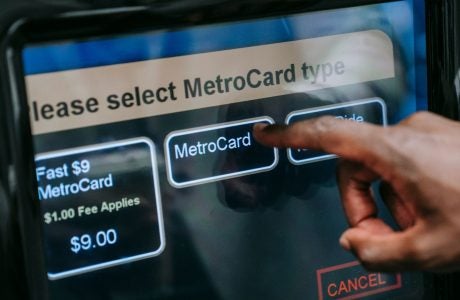 Hand typing on a metrocard machine at a new york subway to pay for a fare.|A person swiping the yellow and blue Metrocard at a new york subway station entrance. Photo of hand swiping the card.