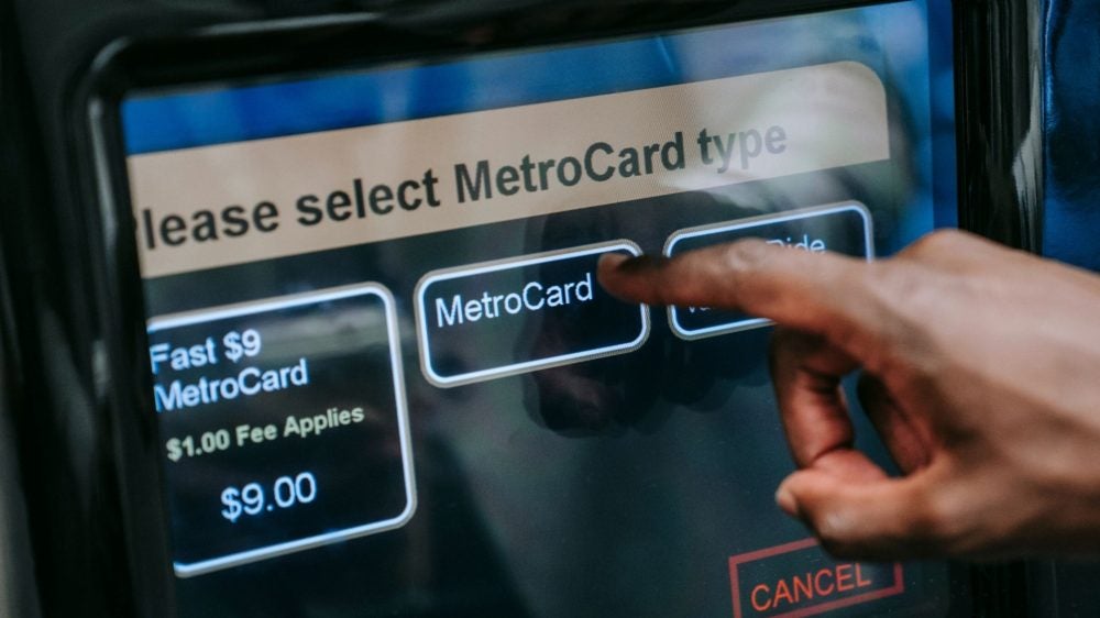 Hand typing on a metrocard machine at a new york subway to pay for a fare.|A person swiping the yellow and blue Metrocard at a new york subway station entrance. Photo of hand swiping the card.