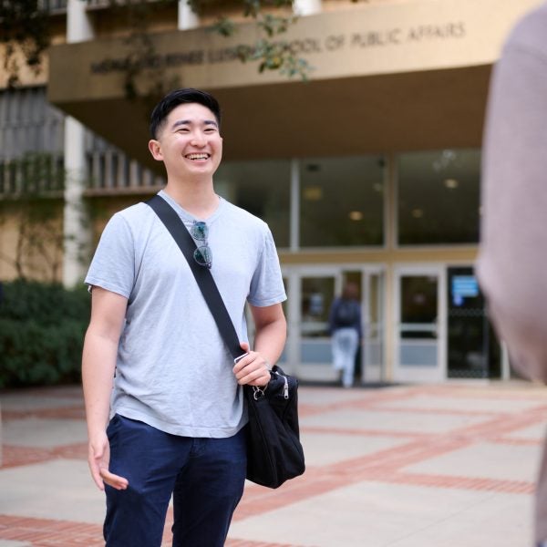 Miles Kim, male Urban planning student stands in front of the Luskin School of Public Affairs building and smiles at friend