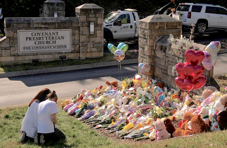 two people kneeling in front of flowers at a makeshift memorial