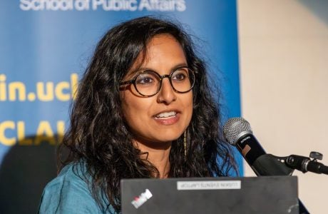 woman with dark hair and glasses speaks from a podium