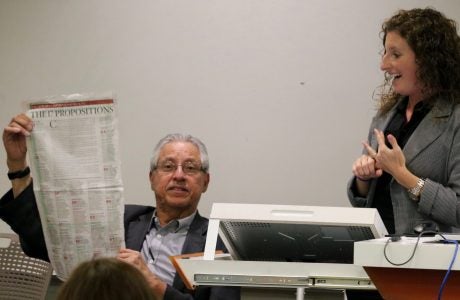 Fernando Torres-Gil, left, holds up a copy of a newspaper article listing the state ballot propositions, as Laura Wray-Lake reacts. Photo by George Foulsham