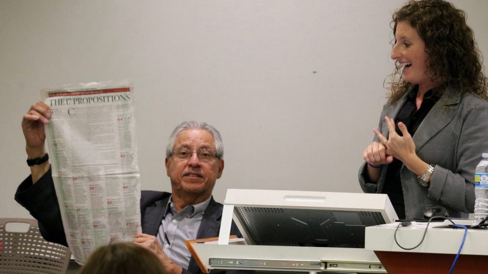 Fernando Torres-Gil, left, holds up a copy of a newspaper article listing the state ballot propositions, as Laura Wray-Lake reacts. Photo by George Foulsham