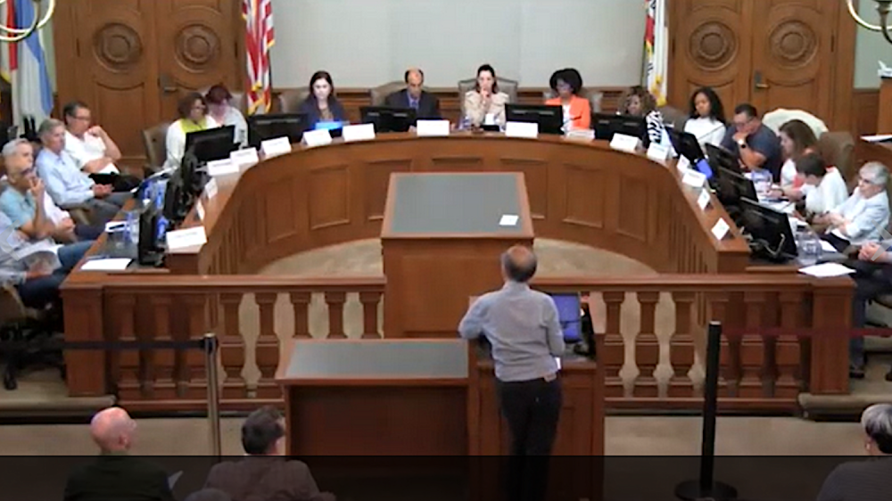 Man at podium addressing officials seated in semicircle