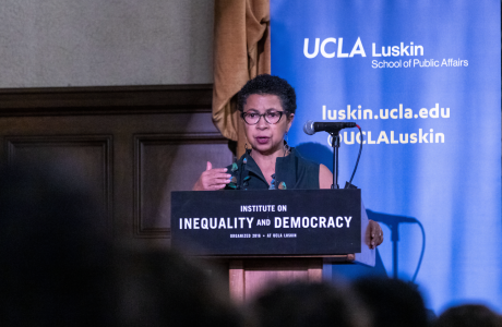 Black woman wearing glasses speaks from a podium with a UCLA Luskin backdrop behind her