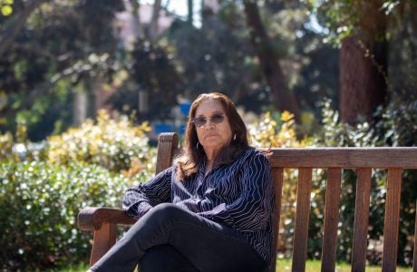 woman in blue top and jeans is surrounded by foliage as she sits on a bench